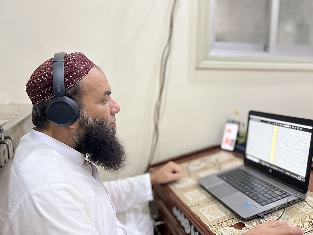 Qari Muhammad Naveed Raja teaching a lesson online, headset on, a page of the Holy Quran open on his screen