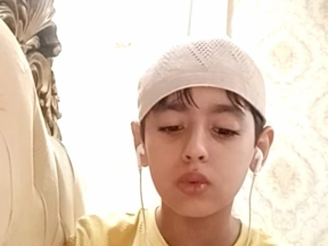 A student in his Quran lesson at home, earphones in, reciting to his teacher on a video call